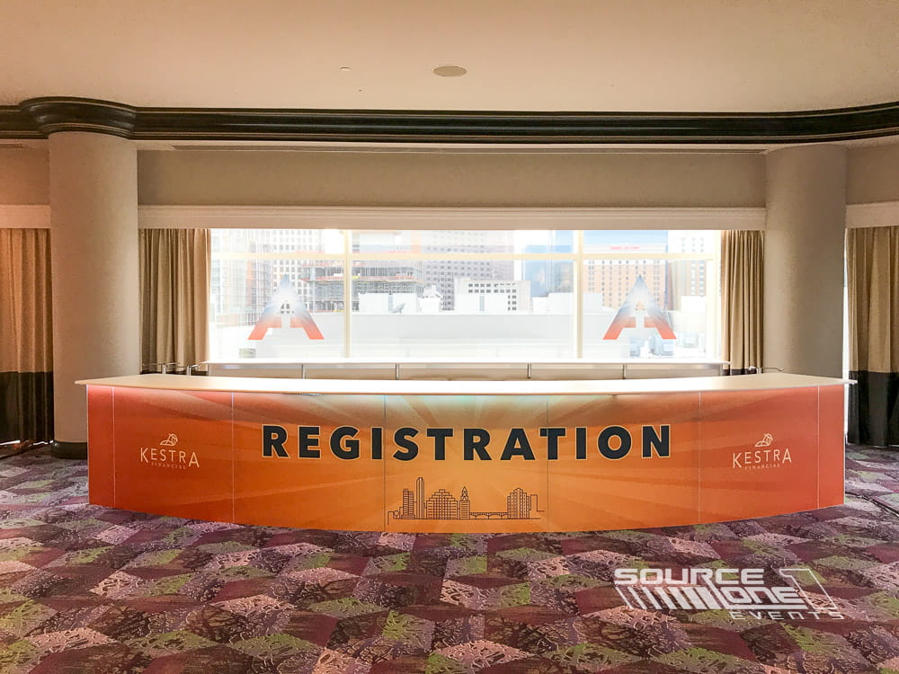 Modern registration desk with clean architectural lines, branded overhead signage, and professional attendee welcome area.