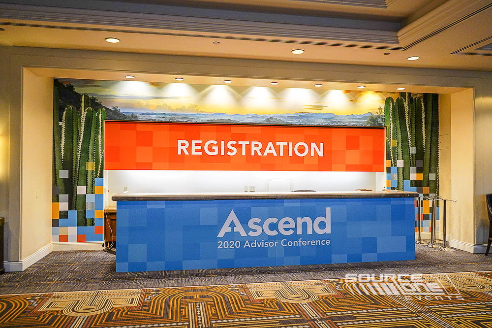 Built-in registration counter with illuminated orange "Registration" signage, warm architectural finishes, and integrated attendee check-in area.