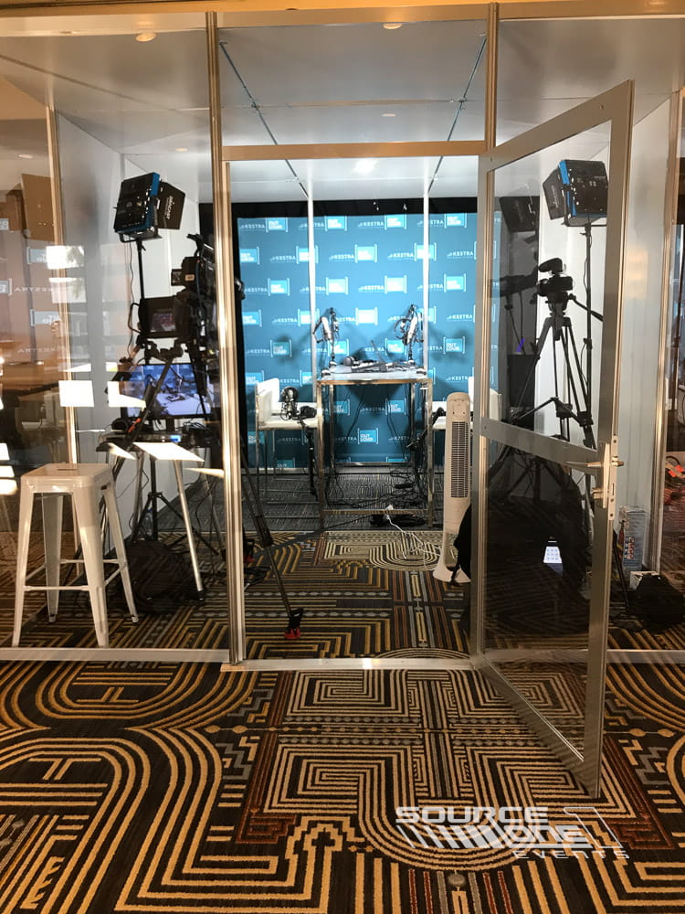 Professional podcast studio featuring glass walls, broadcast equipment, lighting, and branded event production space.
