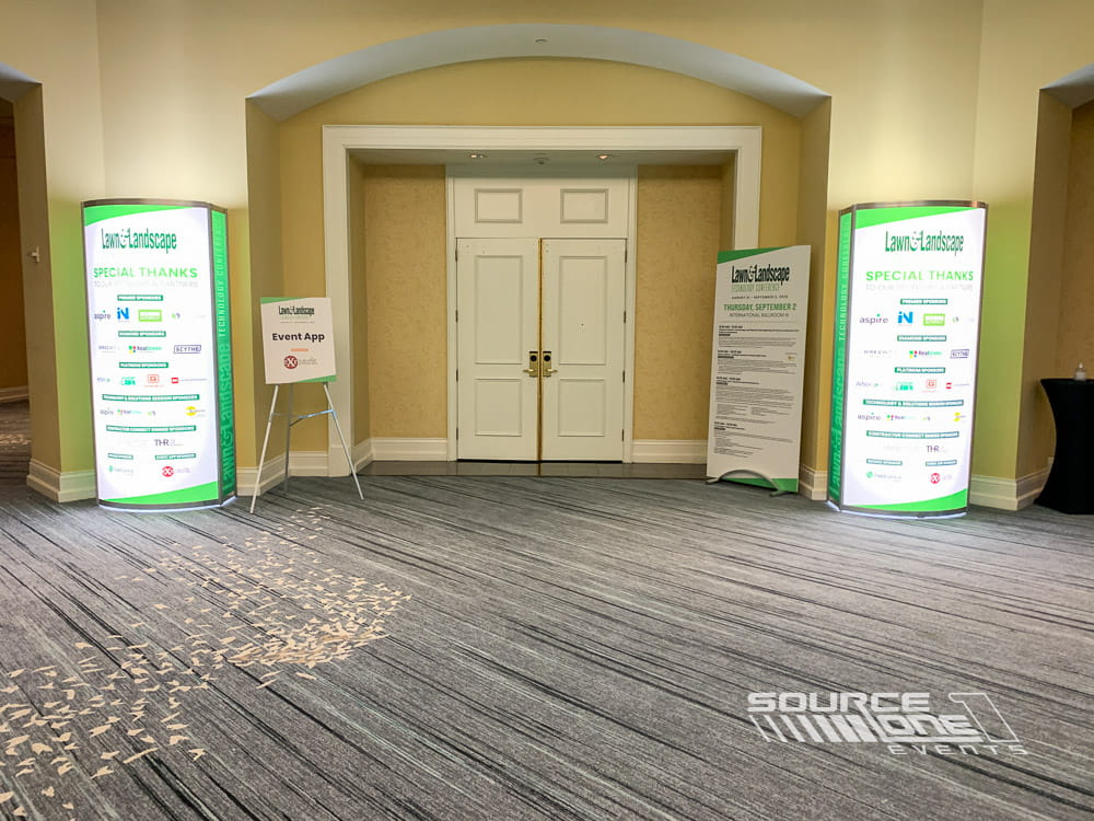 Green illuminated backlit towers surrounding ballroom doors with vibrant conference graphics and attendee wayfinding signage.