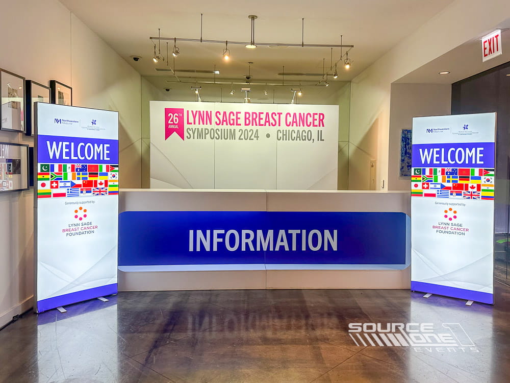 Information and registration counter featuring vibrant pink event branding, digital displays, and attendee welcome services.