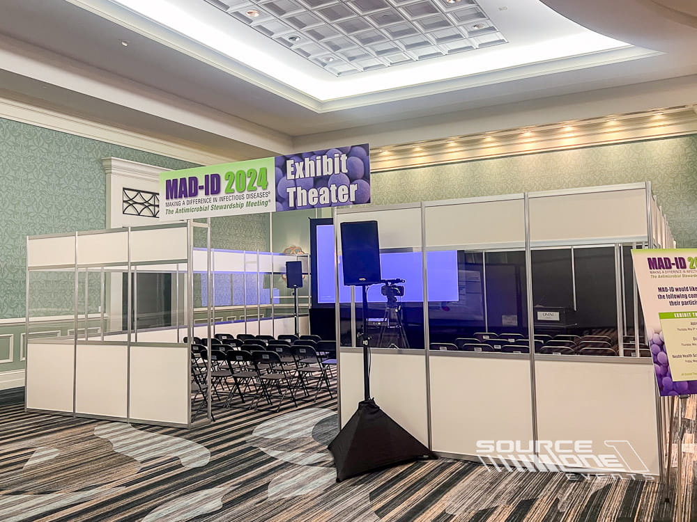 Open exhibit theater with presentation stage, LED screens, audience seating, and educational conference programming.