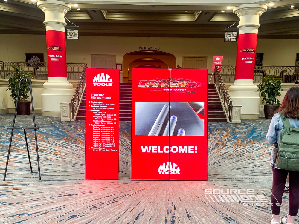 Bright red LED digital poster displays highlighting conference branding and registration information within a convention venue.