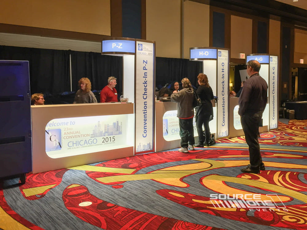 Custom registration counter with navy blue branded backdrop, attendee service stations, and conference check-in area.