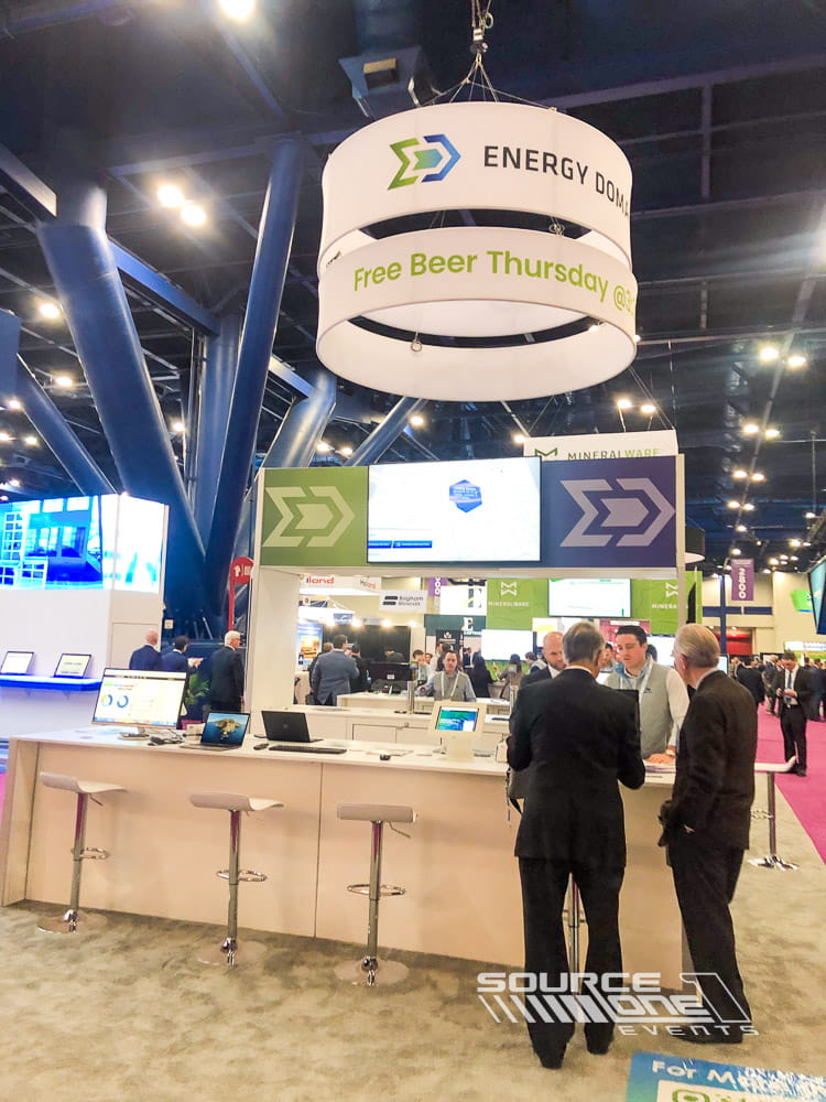 Large custom trade show booth with suspended circular signage, digital media, and premium exhibit architecture.