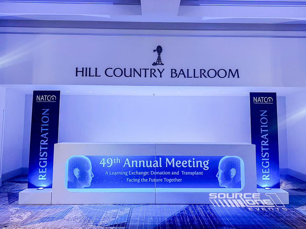 Elegant ballroom registration entrance with blue conference branding, directional signage, and attendee welcome graphics.