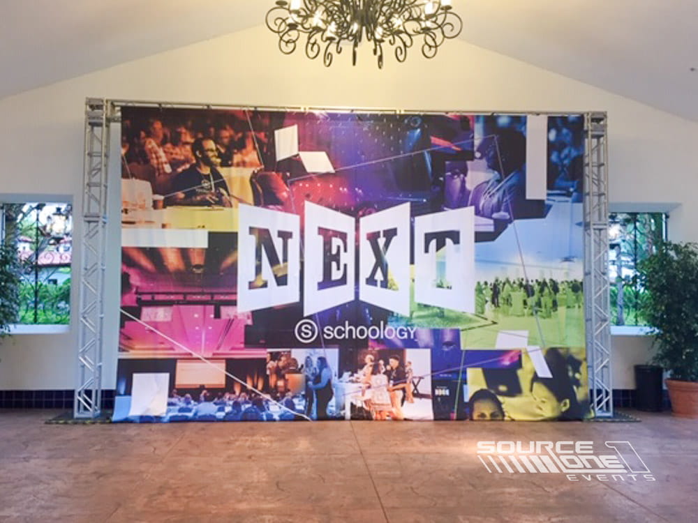 Large branded environmental banner installed across a convention concourse featuring colorful NEXT conference graphics.