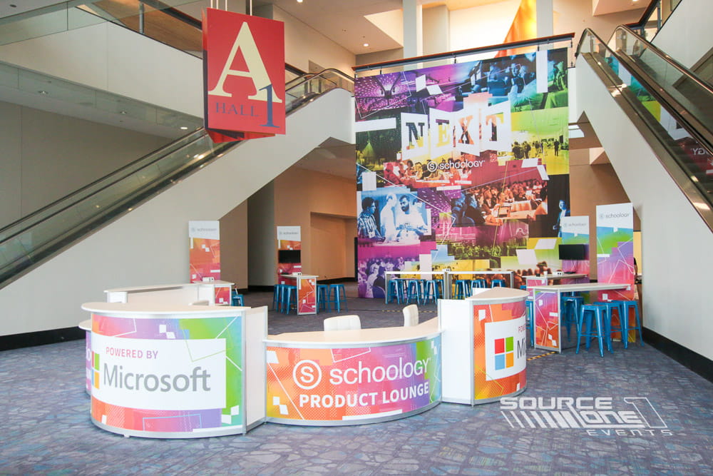 Modern networking lounge beneath colorful suspended signage, designed for attendee collaboration and relaxation.