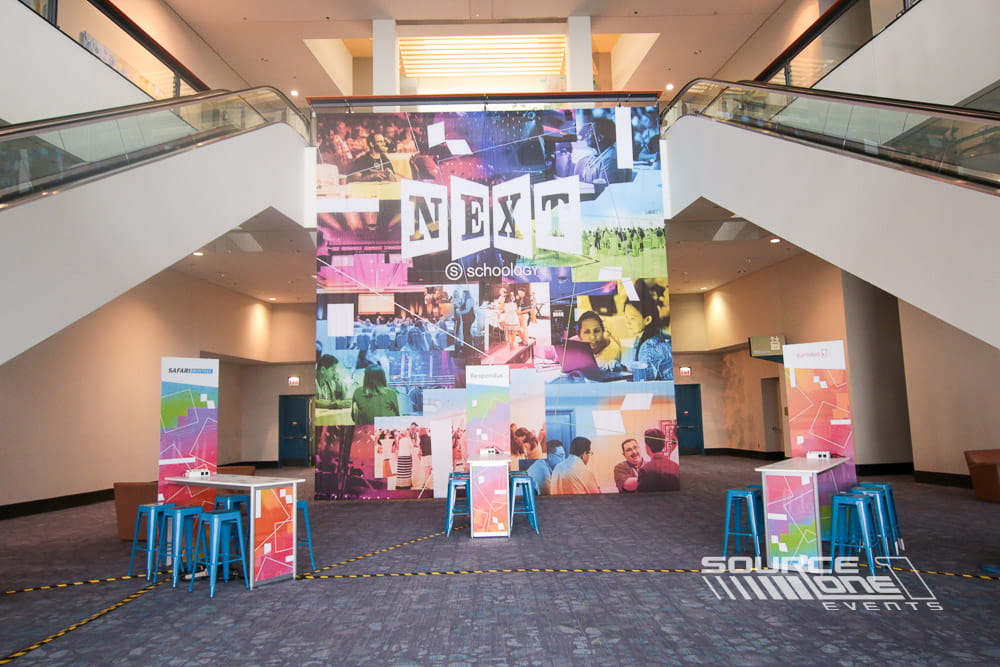 Branded networking lounge positioned adjacent to conference stage areas with colorful graphics and collaborative seating.
