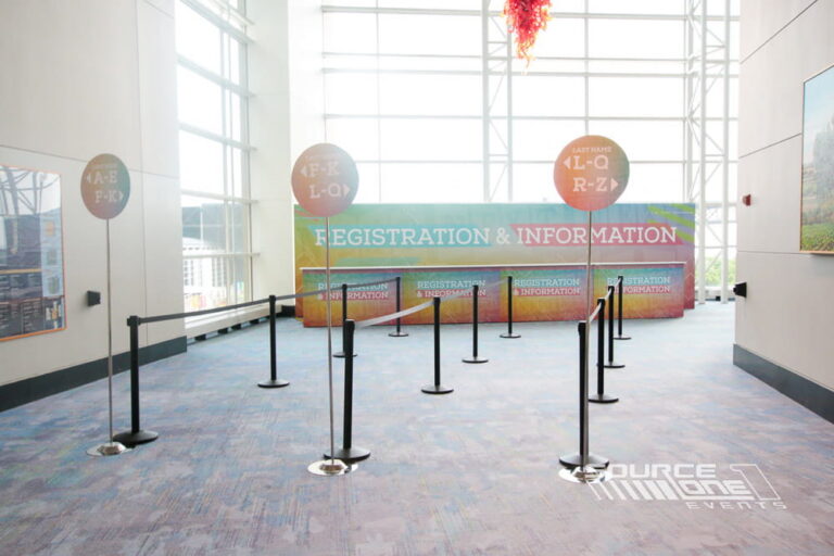 Double-sided circular lollipop signs with colorful event branding directing attendees to registration and information areas.