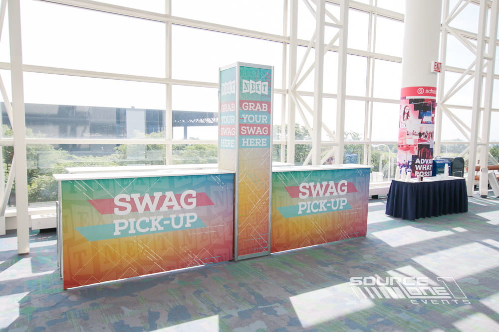 Bright registration information kiosk featuring colorful branding, wayfinding graphics, and natural daylight inside a convention center entrance.