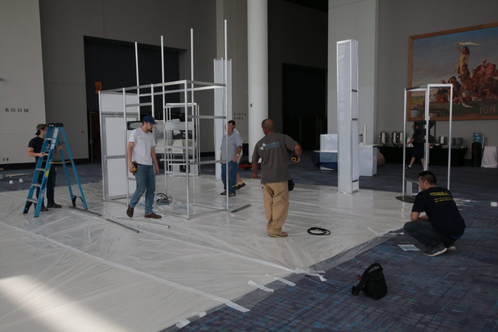 Installation crew assembling exhibit structures inside a convention center before an event.