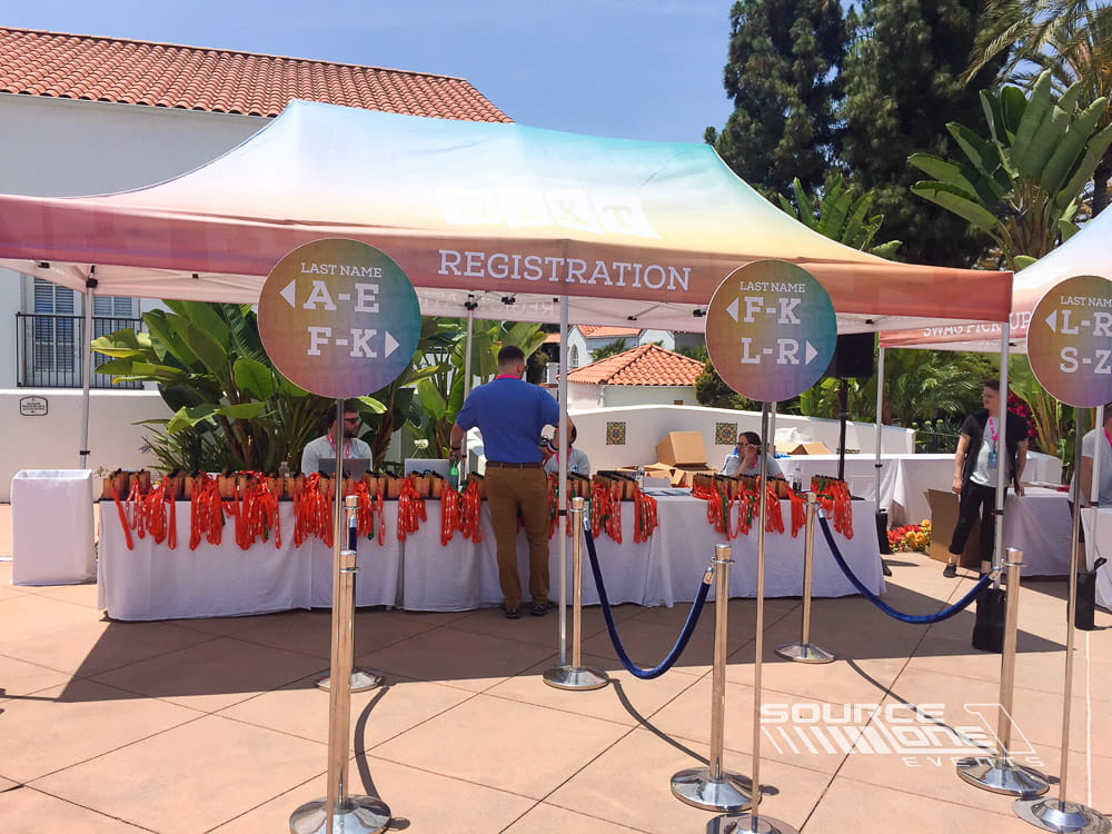 Outdoor event registration tent with branded canopies, colorful signage, and attendee check-in stations for conference arrivals.