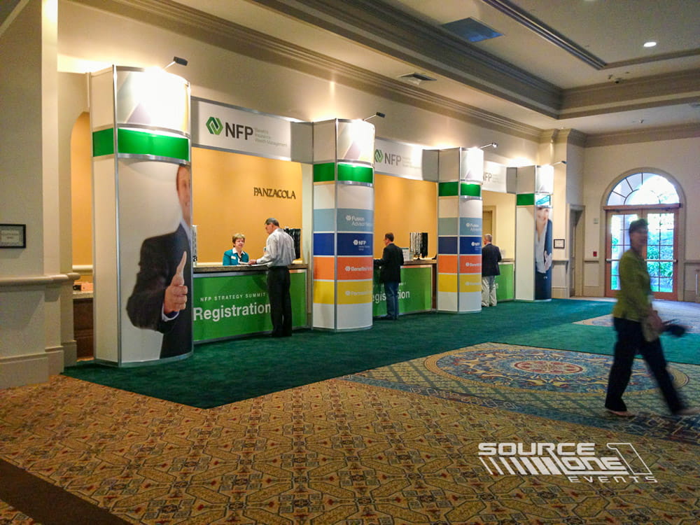 Custom registration counters with green branded graphics, overhead signage, and attendee service stations inside a convention center lobby.