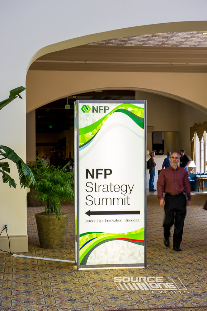 Curved green and white illuminated registration arch with branded conference graphics welcoming attendees.