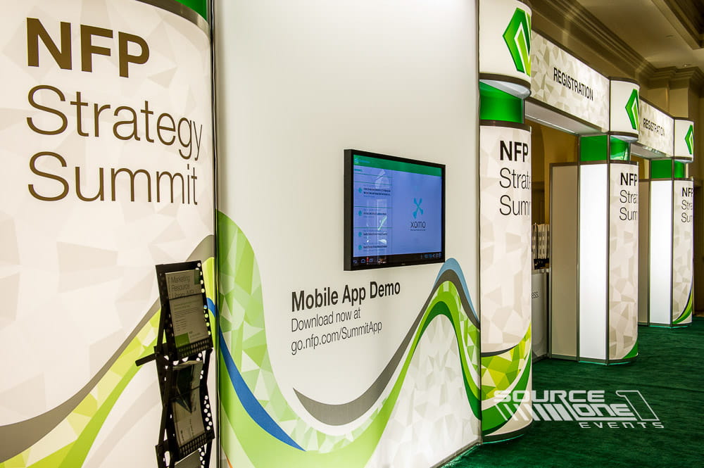Modern conference registration area featuring green and white branded counters, digital information displays, and attendee check-in stations designed by Source One Events.