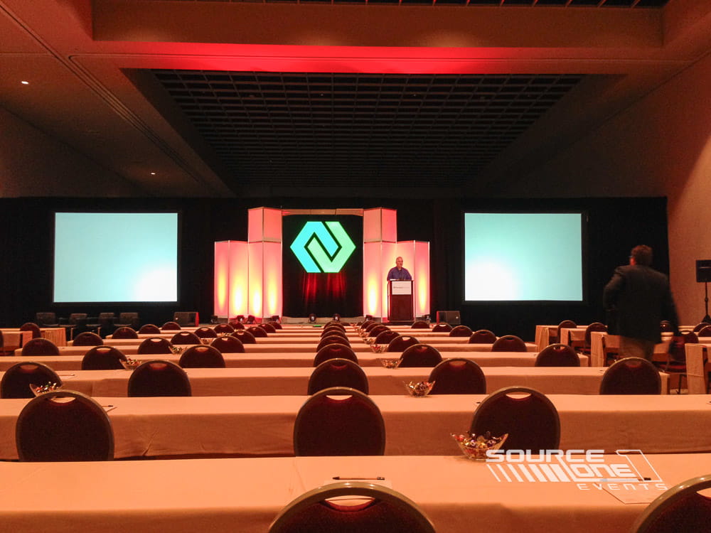 Modern keynote stage with dramatic red and green lighting, dual presentation screens, and audience seating.