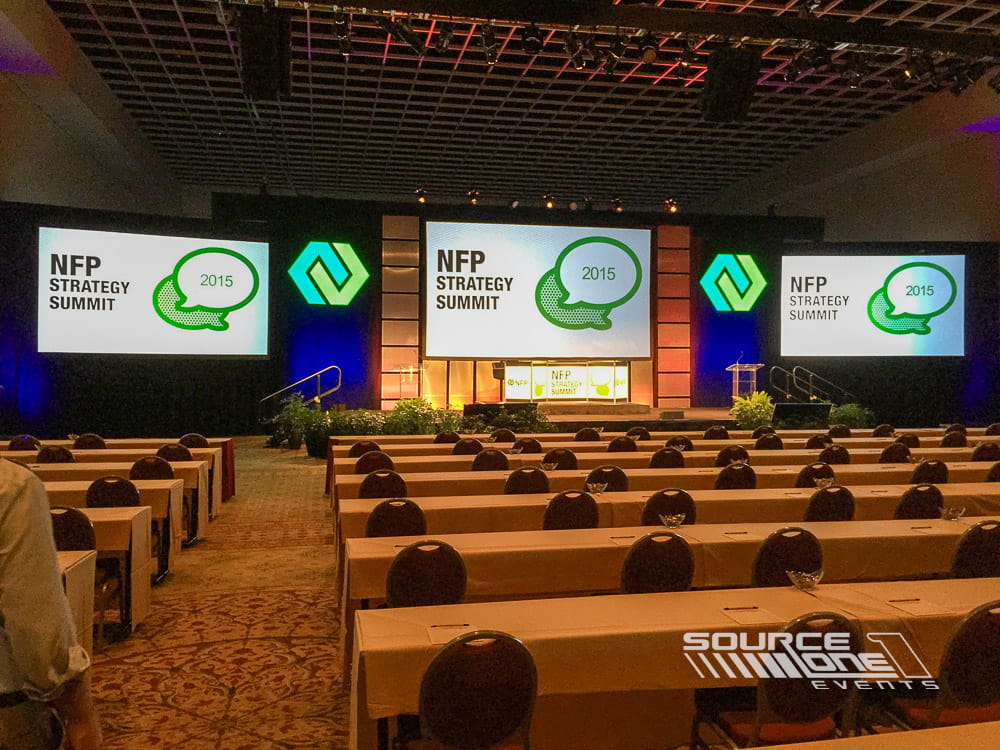 Elegant conference ballroom stage with wood accents, large LED presentation screens, and professional lighting designed for general sessions.