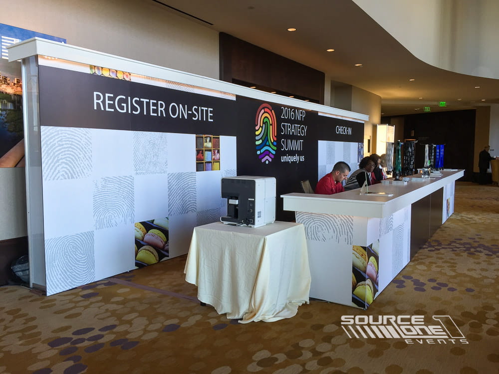 Custom registration counter with black branded graphics, white service desks, and integrated conference wayfinding signage.