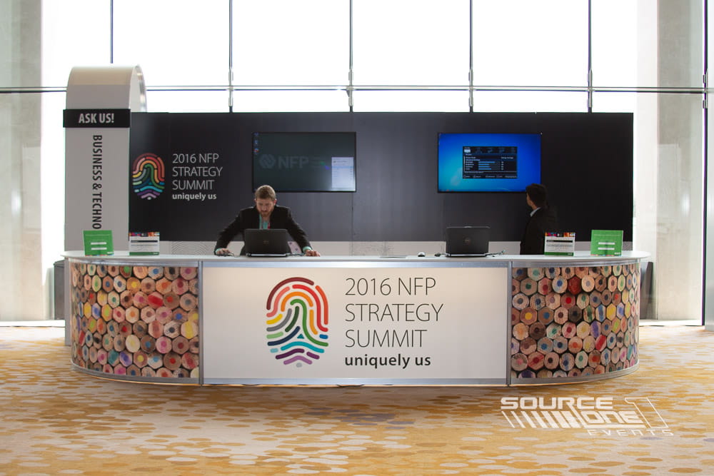 Modern registration area with black and blue branded walls, digital displays, and professional attendee service counters.