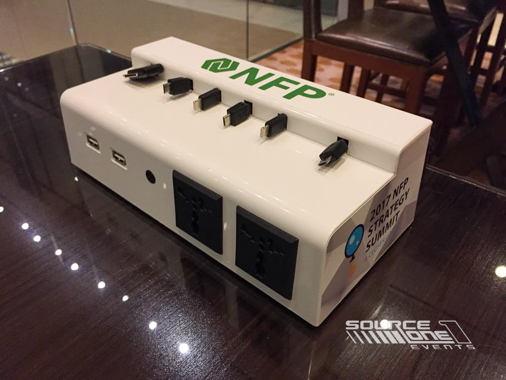 Branded charging station with integrated USB charging ports and custom NFP graphics, providing attendee device charging within a conference networking space.