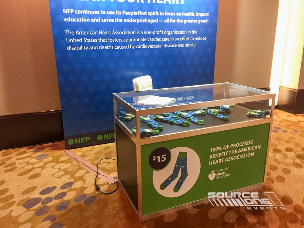Illuminated glass display case showcasing conference memorabilia and branded exhibit materials in a professional event environment.