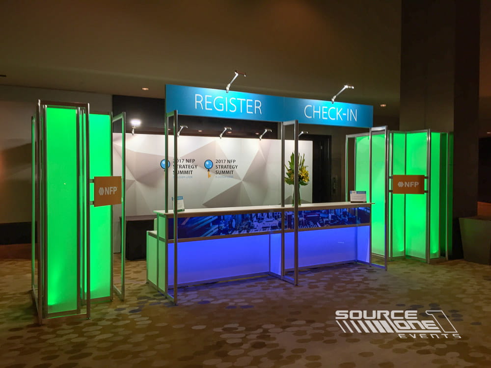 Bright green illuminated registration counter with clean architectural design and branded conference graphics.