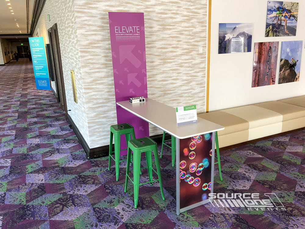 Small networking station featuring branded signage, meeting table, and digital display for attendee engagement.