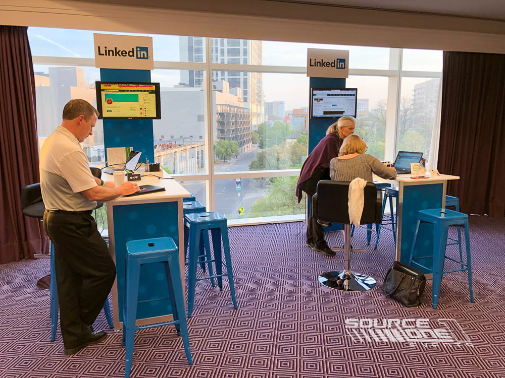 Attendees meeting at networking tables inside a bright conference lounge with exhibitor branding.