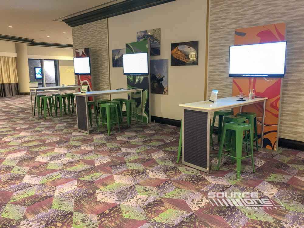 Networking area featuring café tables, branded displays, and collaborative meeting space inside the exhibit hall.