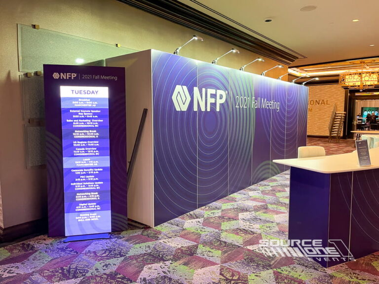 Purple illuminated LED poster tower displaying conference information and sponsor messaging in a hotel convention center.