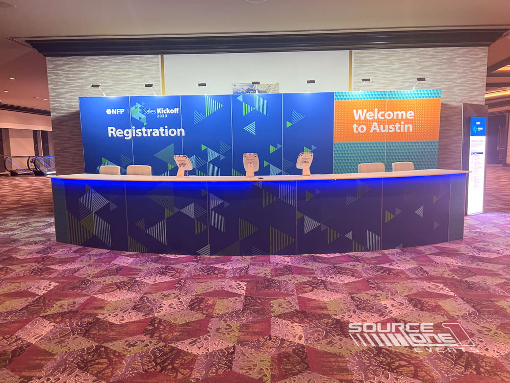 Large registration wall featuring blue corporate branding, multiple attendee service stations, and digital signage.