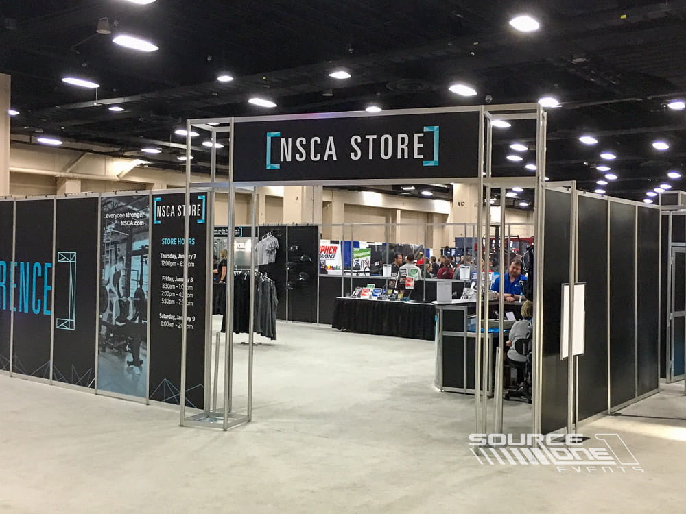 Retail-style merchandise store entrance featuring overhead branded signage and organized shopping experience within the conference environment.