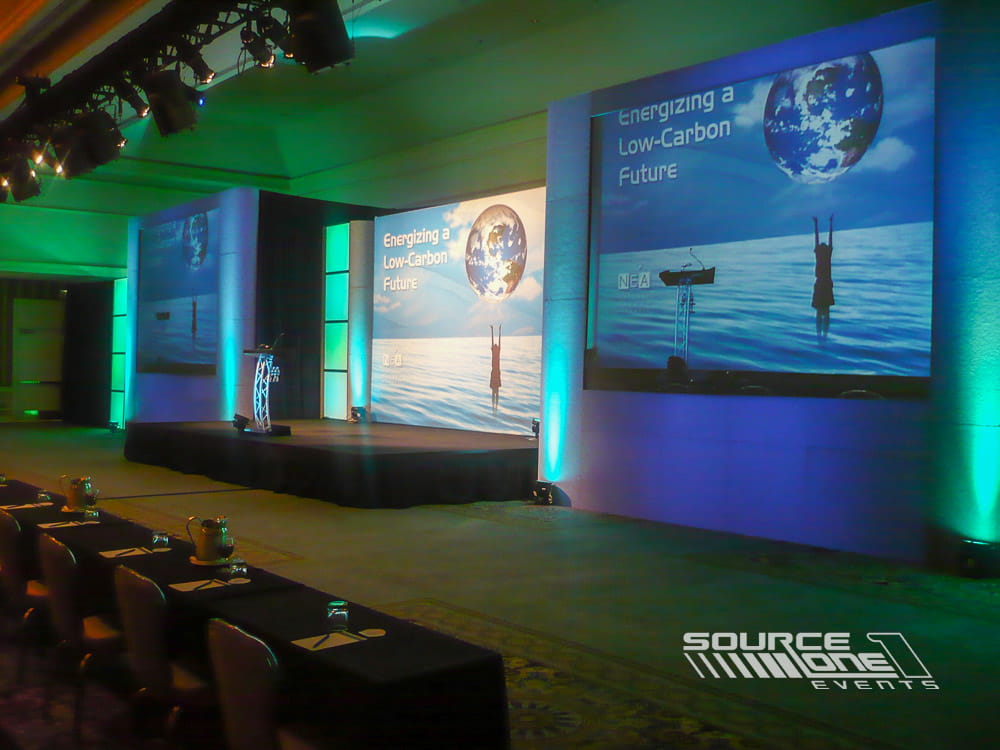 Corporate conference stage illuminated with green accent lighting, scenic backdrop graphics, and professional presentation environment.