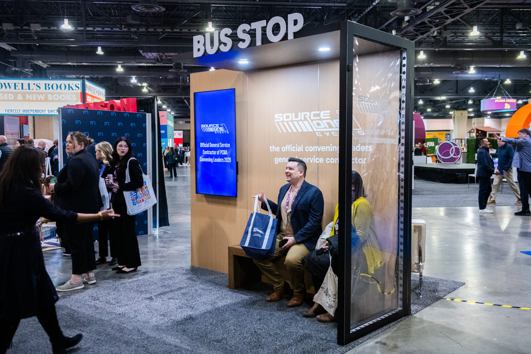 Custom bus stop themed exhibit created by Source One Events, providing attendees with a branded seating area and digital display on a busy trade show floor.