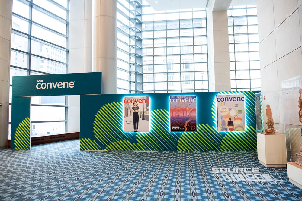 PCMA Convening Leaders networking lounge with teal custom branding, illuminated exhibit walls, and collaborative attendee gathering space designed by Source One Events.