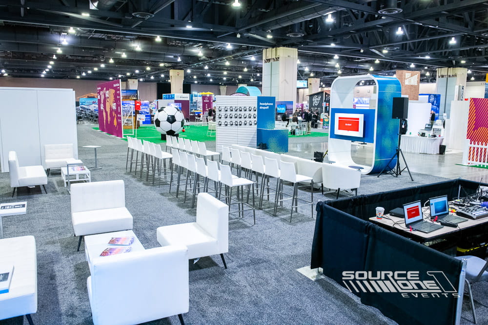 Open conference learning environment with branded stage, modular seating, digital displays, and collaborative attendee engagement area.