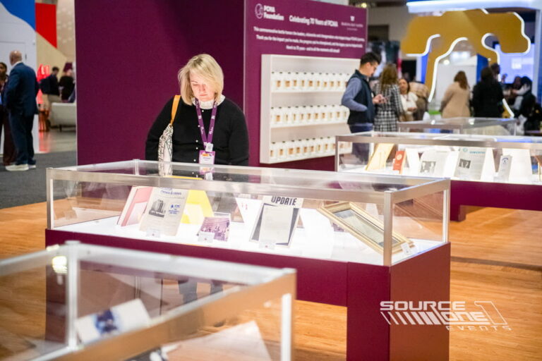 Exhibitor interacting with premium glass display cases used to showcase products and featured exhibits at a trade show.