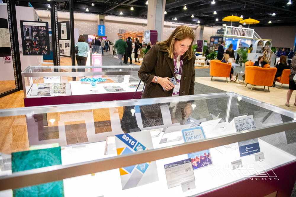 Attendee viewing illuminated display cases showcasing conference exhibits inside the PCMA Convening Leaders exhibition hall.