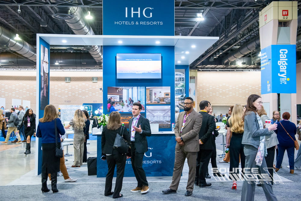 Contemporary IHG trade show exhibit with clean architectural lines, overhead signage, digital displays, and collaborative meeting areas.
