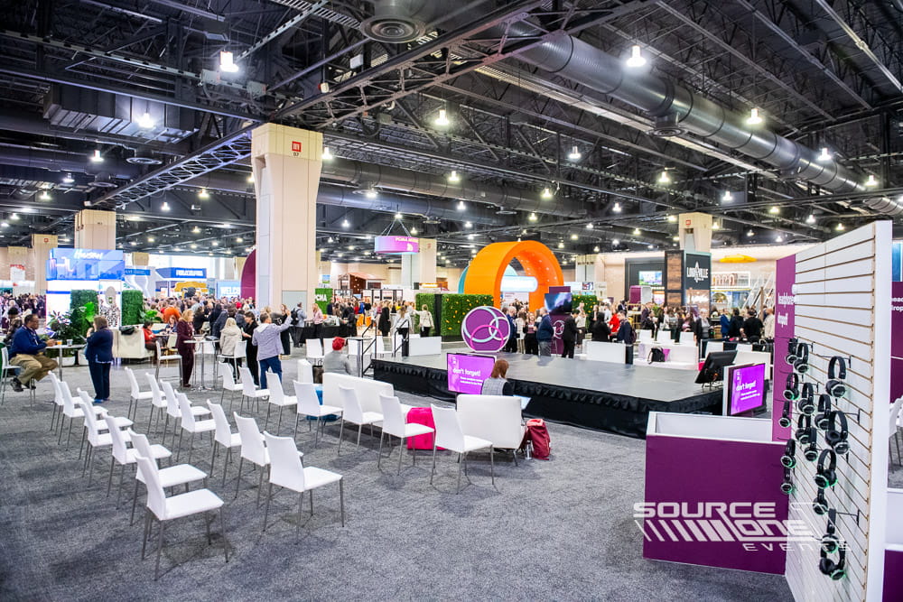 Open educational theater featuring white seating, branded stage graphics, modern lighting, and attendee presentation area inside the exhibit hall.