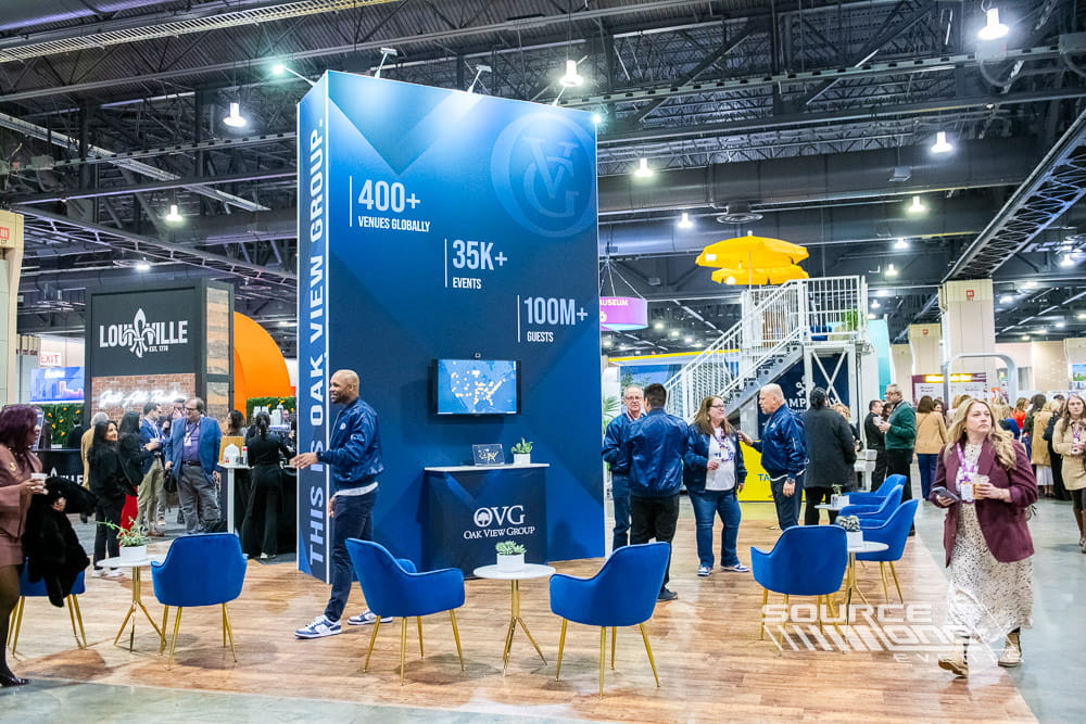 Modern custom trade show booth with blue architectural branding, digital displays, and open meeting areas designed for exhibitor engagement at PCMA Convening Leaders.