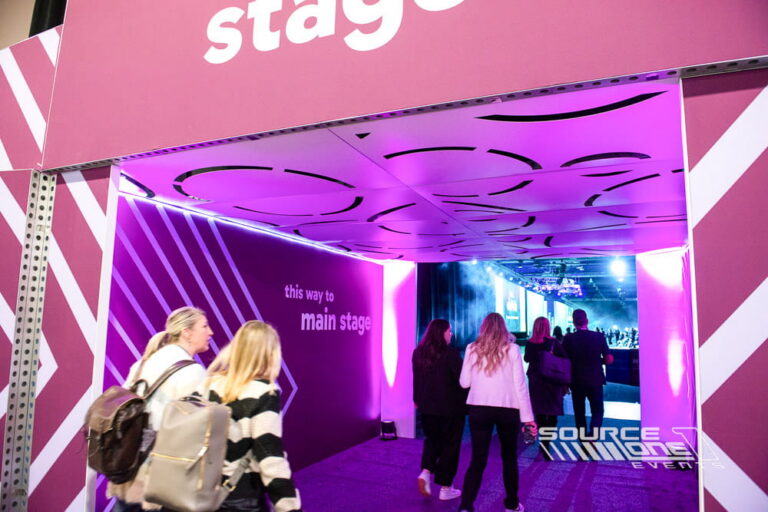 Vibrant purple stage entrance canopy with bold main stage graphics and overhead environmental branding creating a dramatic conference arrival experience.