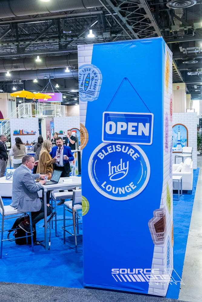 Visit Indy custom exhibit booth featuring blue branded graphics, digital displays, and attendee engagement space on the trade show floor.