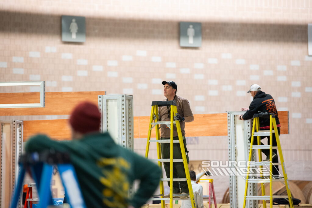 Event technician working from a ladder to install exhibit graphics inside a convention center.