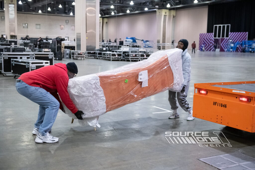 Crew transporting wrapped exhibit materials during convention setup.
