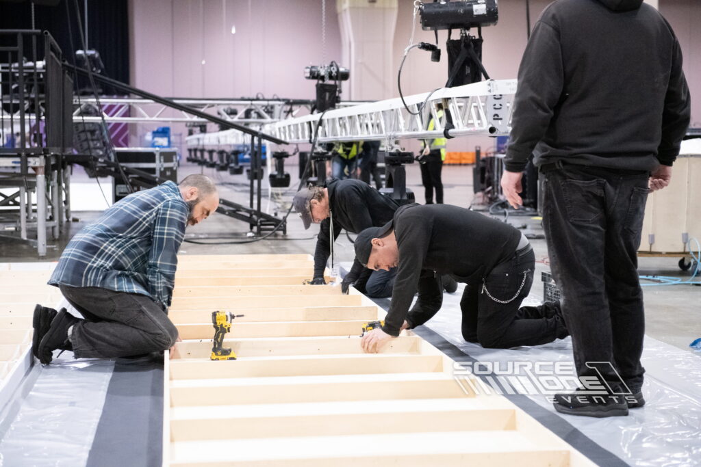 Event technicians assembling exhibit structures inside a convention center.