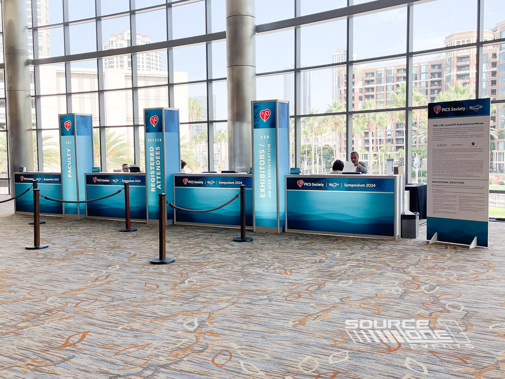 Registration area featuring blue branded counters, digital signage, and natural daylight creating a welcoming attendee experience.
