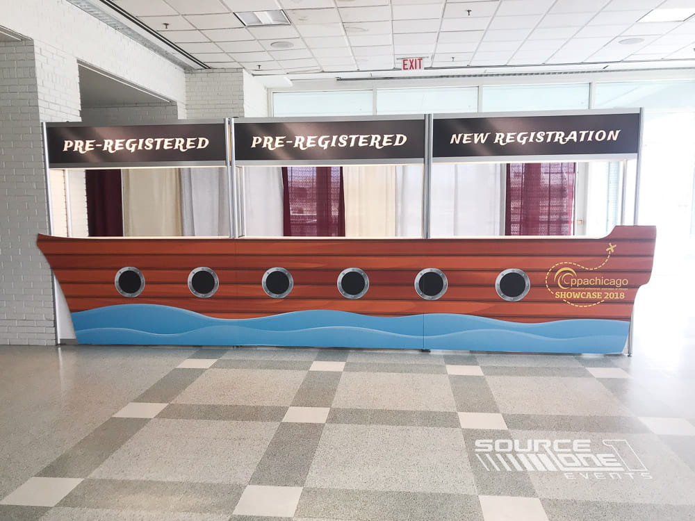 Contemporary registration counter with wood panel backdrop, integrated branding, and attendee service windows.