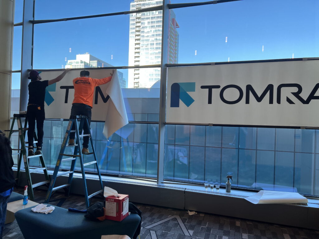 Large custom window graphics installed on a building exterior for event branding.